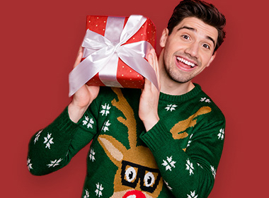 Mann mit Weihnachtspullover hält Weihnachtsgeschenke in den Händen und lächelt